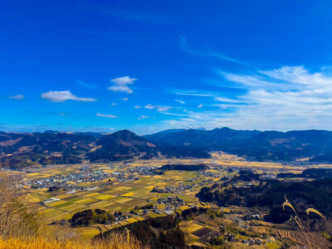 青空と山並みの下に広がる田園風景の展望