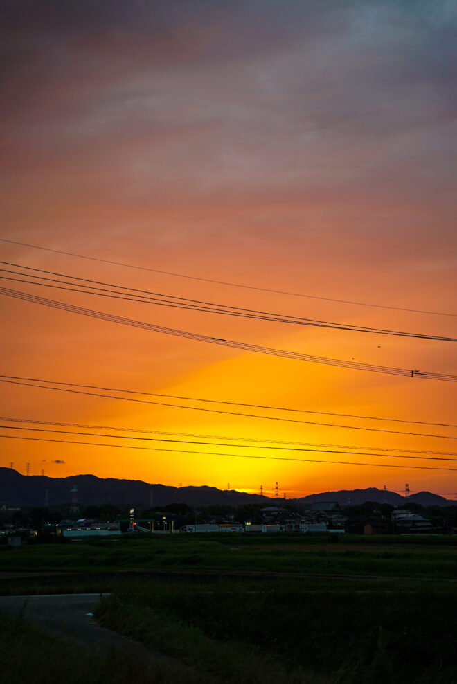 夕暮れに染まる空と電線、遠くに広がる山並み
