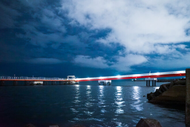 夜の海に架かる赤い桟橋と青い空