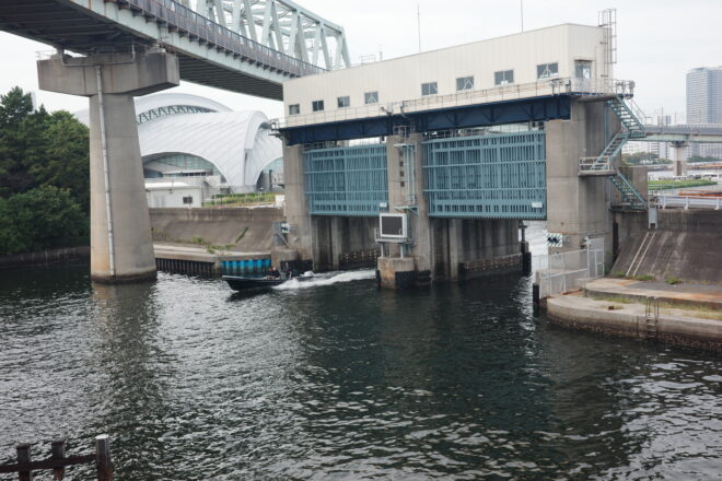 水門や橋脚の下を高速で進む小型ボートを写した、福岡の港湾エリアの写真