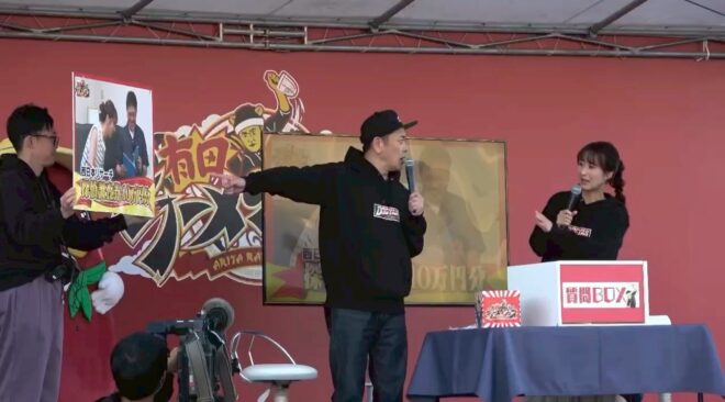 有田ラーメンフェスのステージで、くりぃむしちゅーの有田哲平さんがクローバー探偵事務所の提供する調査券を紹介し、盛り上がる会場の様子。