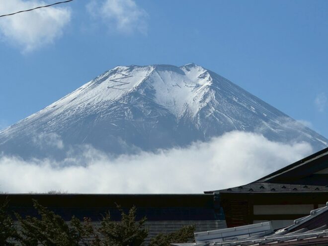 雲海の上にそびえ立つ、雪化粧をした富士山の山頂と手前に見える民家の屋根